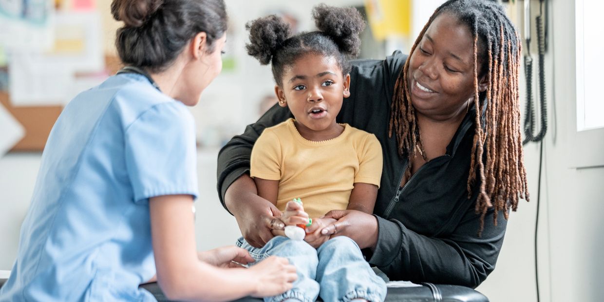 A mother and daughter interacting with a female healthcare professional during a check-up.