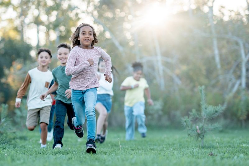 A joyful, diverse group of children runs together in a sunlit park, capturing energy, friendship, and active play. Perfect for family, school, or community wellness themes, highlighting inclusivity and outdoor activity.
