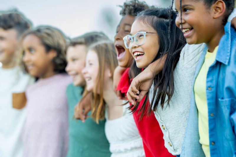 A diverse group of smiling children stands shoulder to shoulder with arms around each other, capturing friendship, unity, and joyful energy outdoors. Perfect for family, education, and community themes.