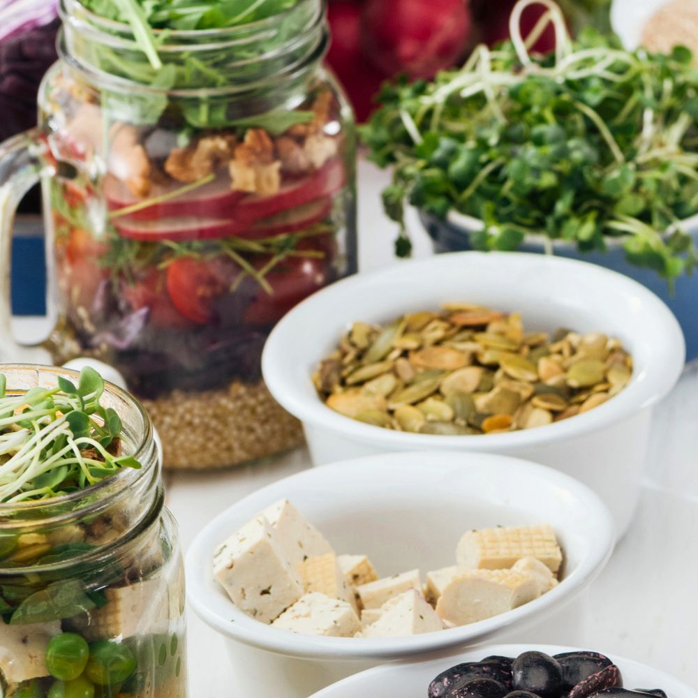 Healthy bowls and jars filled with nuts, seeds, tofu, and fresh greens.