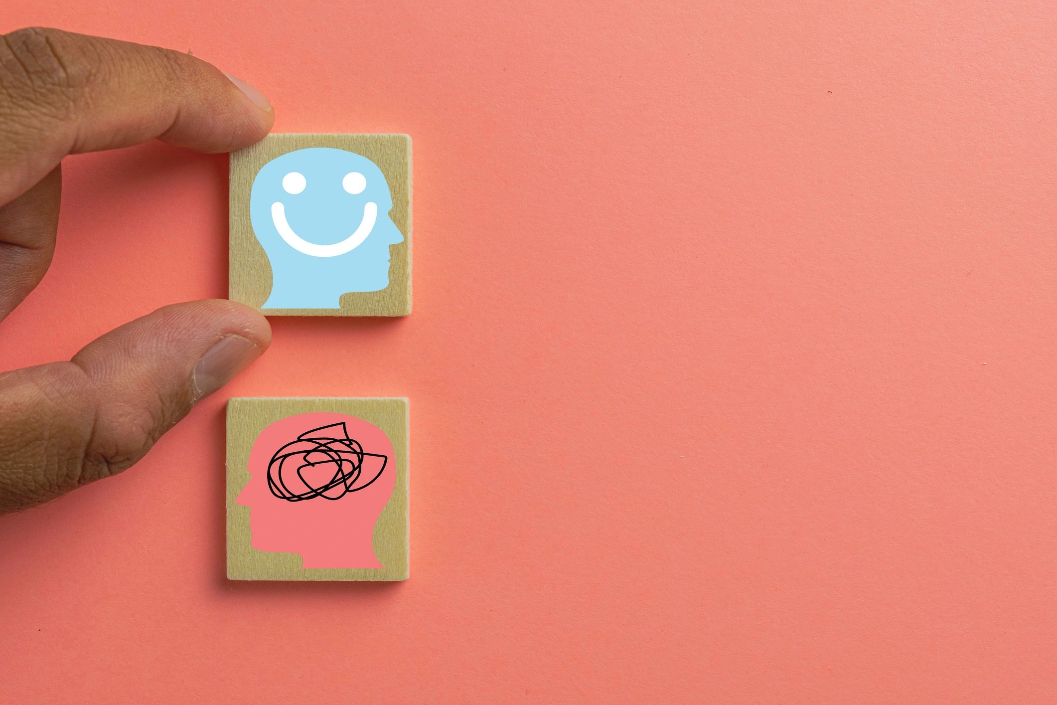 Hand holding wooden block with happy mind icon above block with confused mind icon.