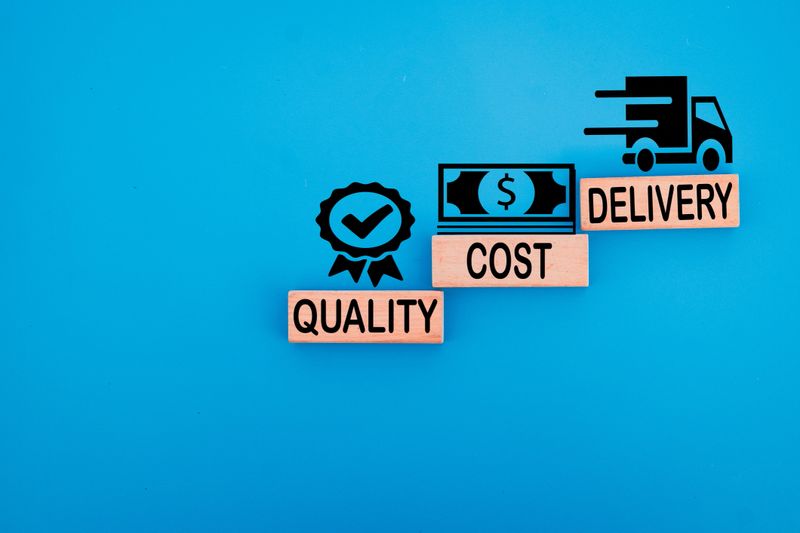 Quality, Cost, Delivery words and icons on wooden cubes over blue background with copyspace idea for supply chain management, business efficiency, logistics strategy, and operational excellence.