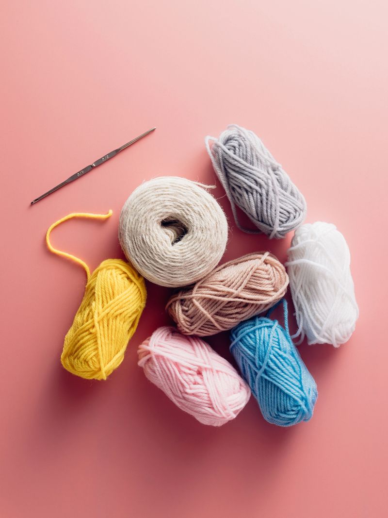 A vibrant arrangement of colorful yarn spools and a crochet hook on a soft pink background, perfect for crafting and creative art projects.