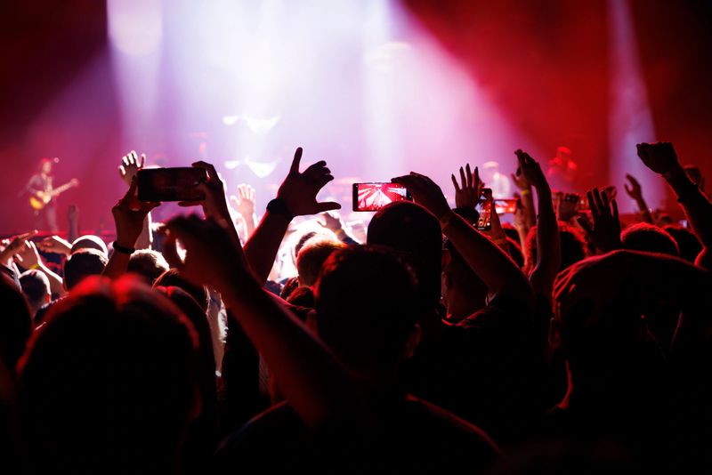 A lively crowd raises hands during a live rock concert with vibrant red stage lighting.