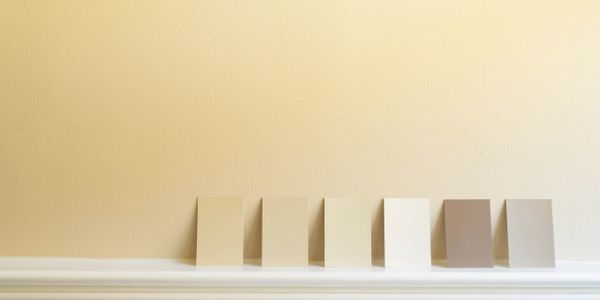 Six paint sample cards lean against a beige wall above white molding.