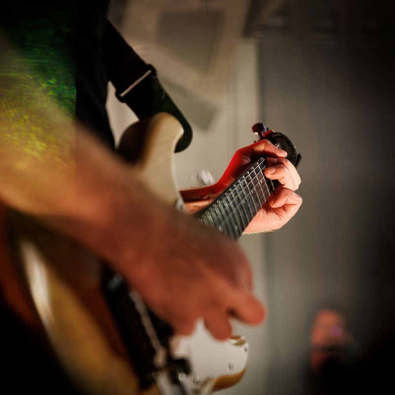 Guitaristâs fingers on fretboard during energetic stage performance. Great for music, entertainment, and creativity themes.