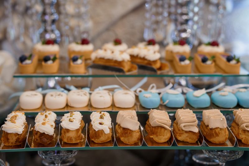 A lavish tiered dessert display features rows of delicate pastel-colored mini cakes and cream puffs adorned with fresh berries, representing an upscale wedding feast