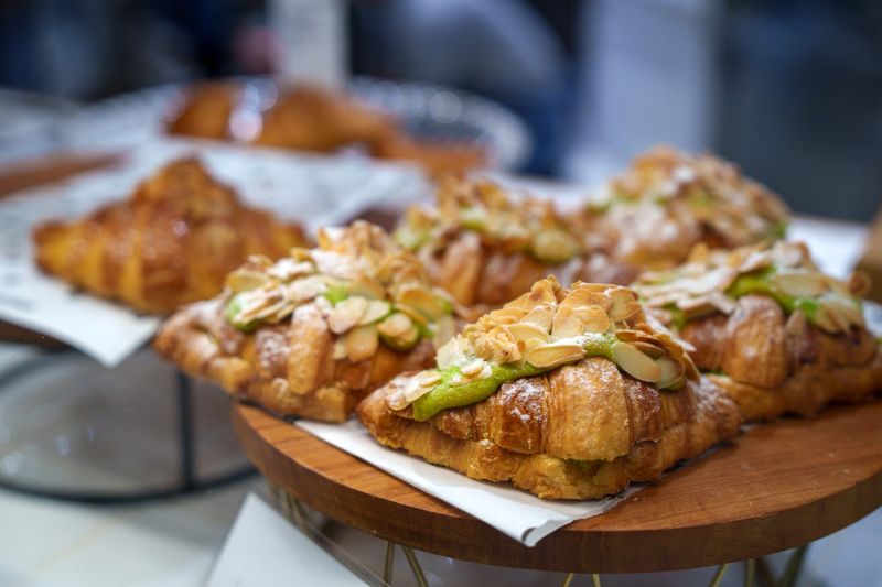 Freshly baked almond croissants arranged on a wooden stand in a bakery setting.