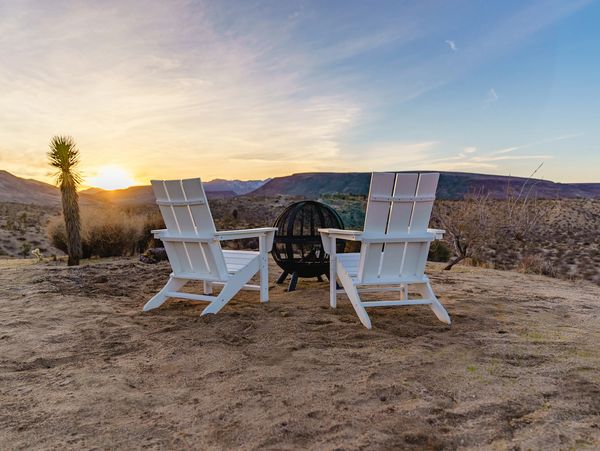 White Adirondack chairs around a fire pit at sunset.