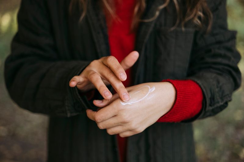Person applying nourishing hand cream to protect skin from dryness. Natural skincare and self-care routine in cold season, soft daylight, close-up outdoors.