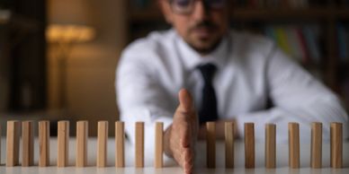 Man stopping domino effect with his hand, symbolizing intervention.