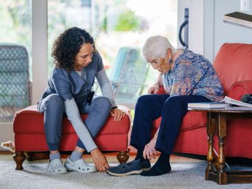 Caregiver assisting elderly woman with footwear at home.
