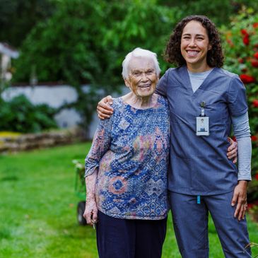 Elderly woman and smiling nurse standing together outdoors.