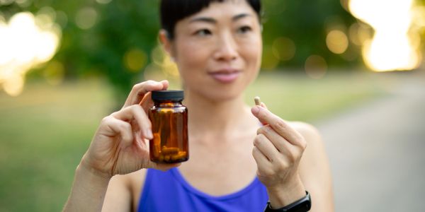 A woman holding a pill and an amber medicine bottle outdoors.
