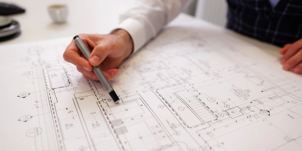 Person working on architectural blueprints with a pen.