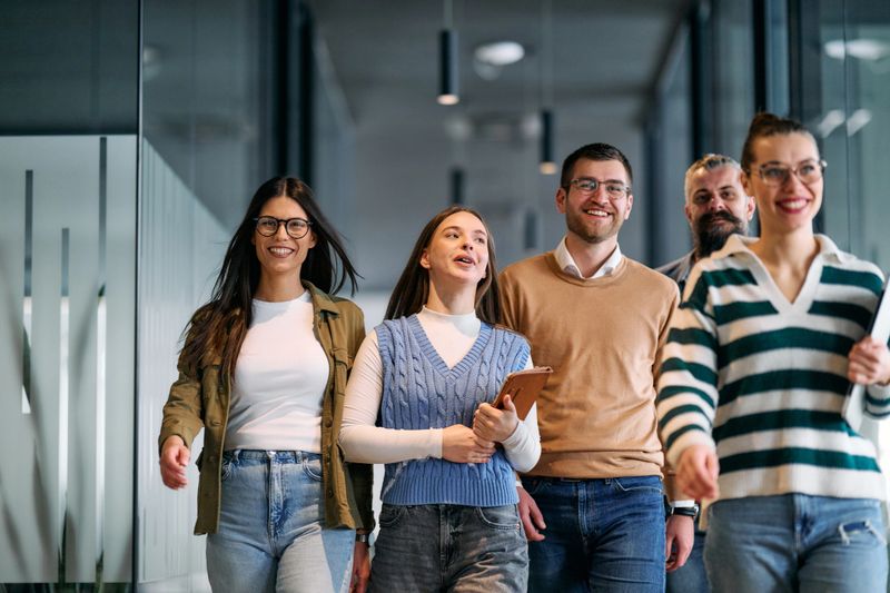Group of young business team walking together through a modern office hallway, smiling and discussing work. Concept of confidence, teamwork, leadership, and positive workplace culture