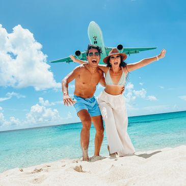 Couple posing excitedly on the beach with a plane overhead.