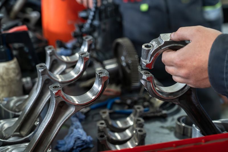 Mechanic holding shiny connecting rod at engine repair workshop, showcasing precision engineering, automotive maintenance, industrial tools and mechanical work process.