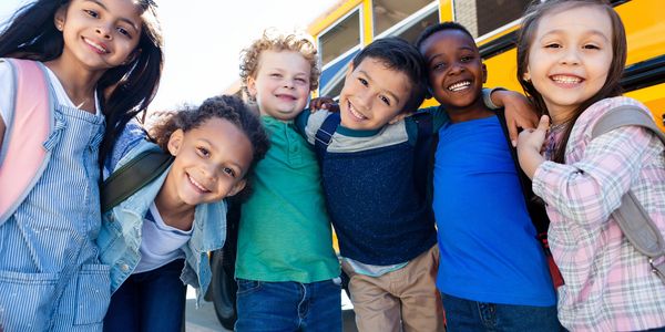 Group of joyful diverse kids hugging closely by a yellow school bus