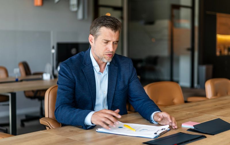 Mid adult businessman concentrating on reports and data, planning strategies during an important meeting indoors