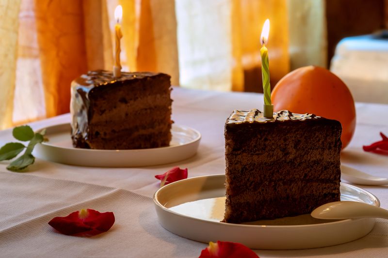 Two slices of chocolate cake with lit candles on plates.  Dessert for birthday celebration. Holiday food and sweet treat concept.
