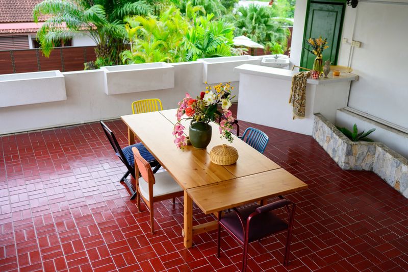 High view of a cozy semi-outdoor dining area with a wooden table, assorted chairs, and a floral centerpiece—perfect for enjoying tropical views