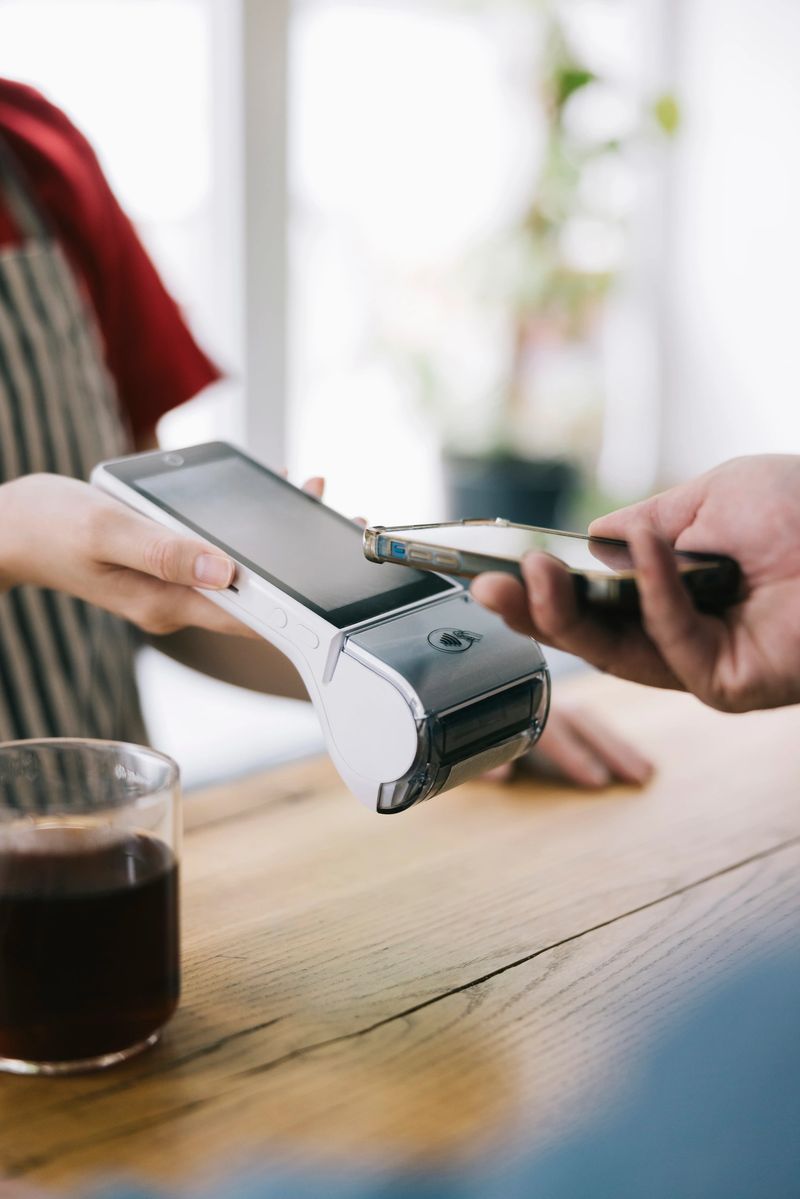 A secure and convenient contactless payment is made using a smartphone. The image captures the technology of wireless payments in a casual cafe setup with coffee on a wooden table.