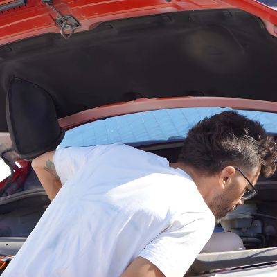 Man inspecting the engine of a red car.
