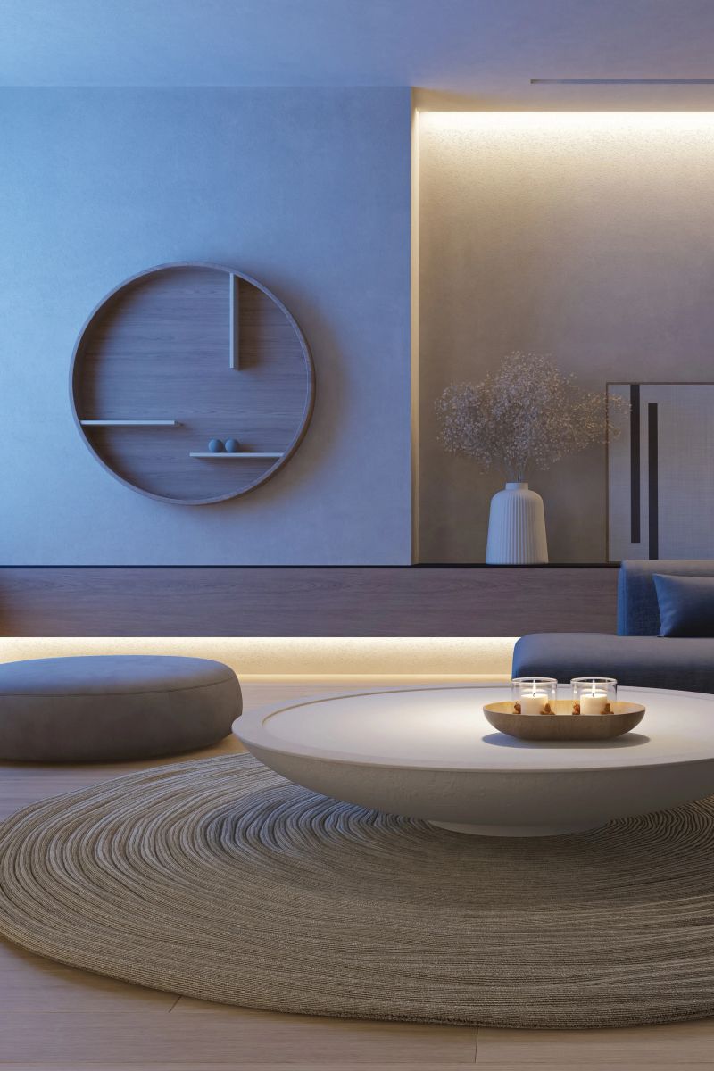 A blue hour night interior view of Japandi-inspired living space that blends the simplicity of Japanese design with the warmth of Scandinavian aesthetics. The interior features a refined mix of natural materials—concrete, stone, pine wood, and soft textiles—arranged with clean lines and understated elegance. Subtle LED lighting is integrated into architectural details, casting a warm glow during dusk or blue hour and enhancing the tranquil ambiance. Close-up elements such as circular forms, organic textures, and neutral tones contribute to a sense of balance and mindful living. This image is ideal for illustrating minimalist home design, editorial features on wellness-focused interiors, or visual content promoting sustainable architecture and contemporary lifestyle aesthetics.