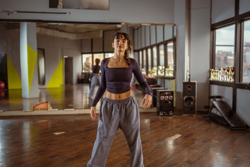 Young woman dancer posing in a modern dance studio, expressing confidence and freedom while practicing her hip-hop moves, with reflections in large mirrors and city views from expansive windows