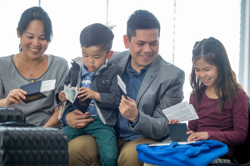 A cheerful Asian family of four sits together, checking passports and travel documents. The mother, father, son, and daughter smile as they prepare for an upcoming trip, showcasing unity and family connection.
