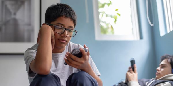 Two boys sitting indoors, focused on their phones.