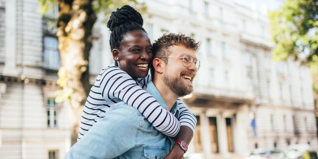 Happy couple enjoying a piggyback ride outdoors in an urban setting.