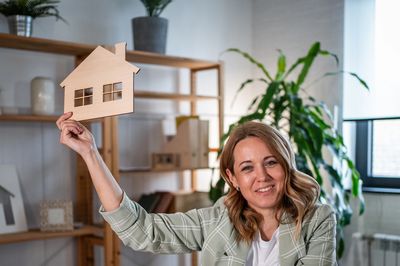 Smiling woman holding a wooden house model indoors.