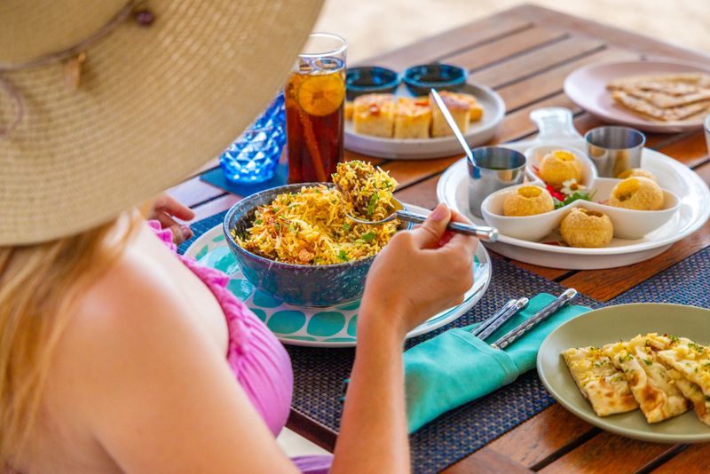 Woman enjoying Indian cuisine outdoors, featuring biryani, appetizers, bread. Casual dining, summer setting, vibrant colors. Leisure, travel, gastronomy, lifestyle concept.