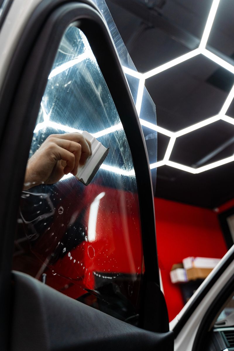 Smoothing dark tint film on side windows removes air bubbles and ensures perfect alignment. Detailer apply dark tint film to car side windows using a squeegee for smooth, bubble-free adhesion