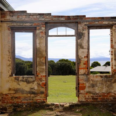 View through a dilapidated brick wall to a green field and distant mountains.