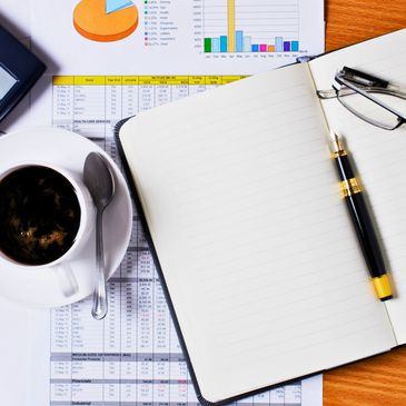 Coffee cup, open notebook, pen, and glasses on financial charts.