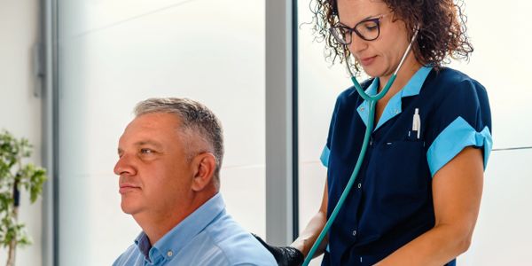 Nurse using stethoscope to check older man's back in a clinic.