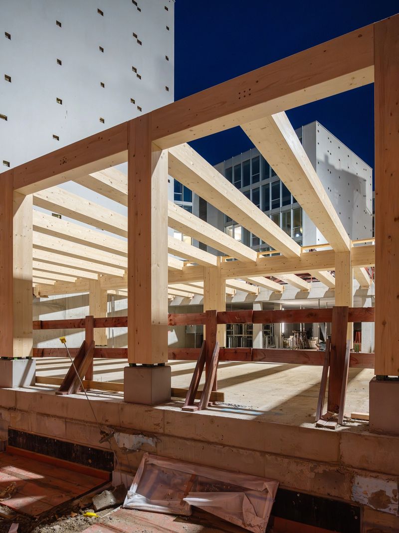 Modern building construction site at night with exposed timber beams and structural framework illuminated by artificial light
