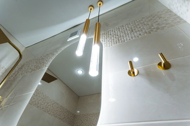 This stylish bathroom features a round mirror above the sink and two stunning light fixtures from the ceiling, creating a warm, inviting atmosphere that enhances the overall design