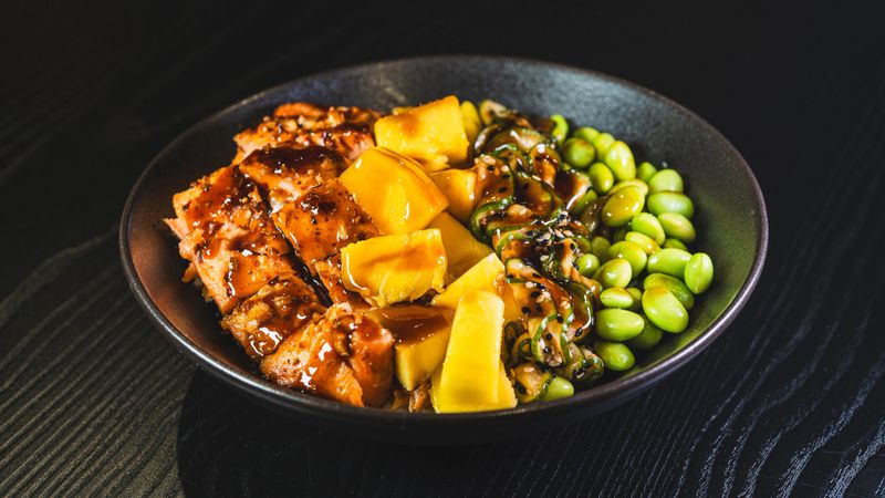 Beautiful grilled salmon poke bowl with mango, sunomono salad, edamame, and glossy sweet-teriyaki sauce. A delicious fusion of Hawaiian and Japanese flavors in one bowl.