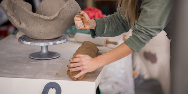 Person shaping clay on a table in a pottery studio.