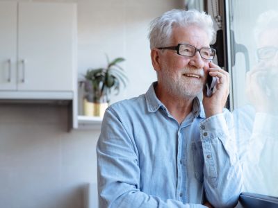 Elderly man smiling while talking on phone by the window.