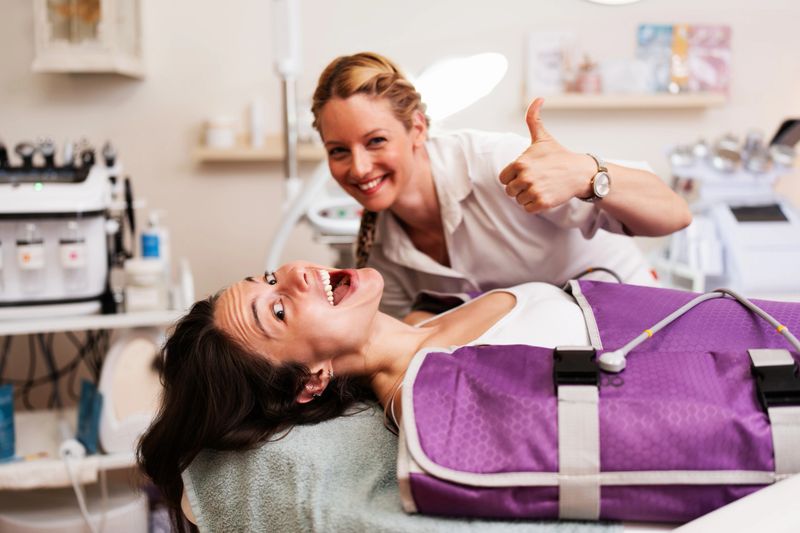Woman receiving an aesthetic pressotherapy treatment on her legs in a modern beauty salon while the female aesthetician gives a happy thumbs up gesture