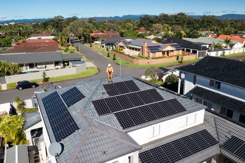 Solar panels and technician on luxury waterfront home on a sunny day.