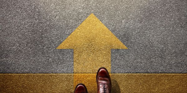 Person standing with brown shoes near a yellow arrow pointing forward.