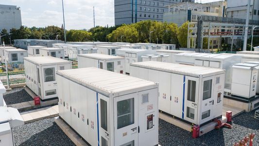 Energy storage containers with wind turbines in the background.