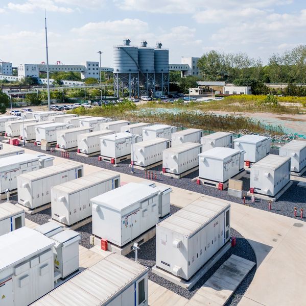 Rows of large industrial white containers or units in an outdoor facility under a partly cloudy sky.