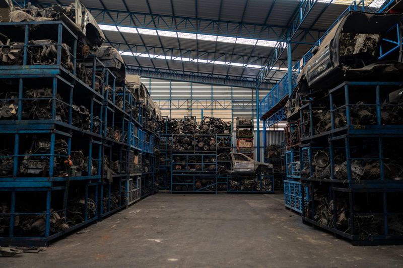 Large industrial warehouse filled with stacked metal shelves containing used automotive parts, engines, and vehicle components for recycling